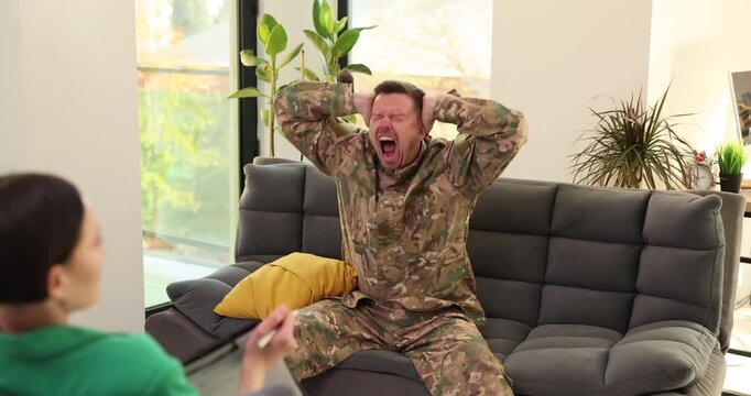 veteran in camouflage explodes with emotion on couch while therapist watches, arms flailing and face contorted intense outburst