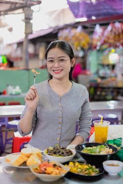 Cheerful woman enjoying delicious street food at a vibrant outdoor market in the evening