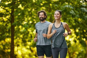 A man and woman jog side by side along a winding path surrounded by vibrant greenery, showcasing their commitment to fitness and enthusiasm for outdoor activities on a sunny afternoon.