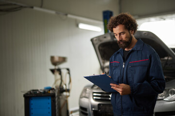 A car mechanic is focused on evaluating the condition of a vehicle in a repair shop. He is checking...