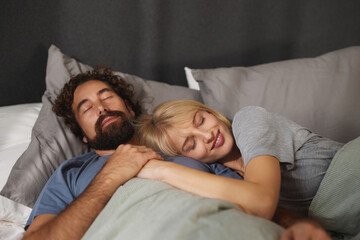 Two people lie comfortably in bed, sharing an intimate moment of sleep. They are nestled closely,...
