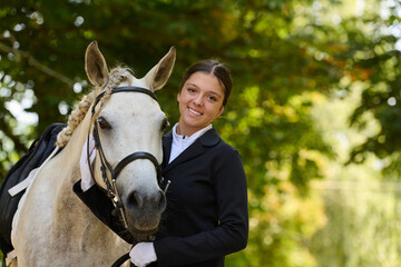 Smiling equestrian woman with her white horse in a natural outdoor setting, horse riding and...