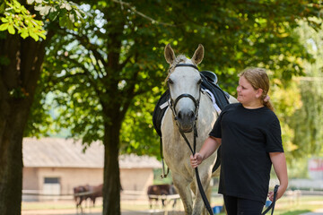 Girl leading a white horse outdoors, equestrian lifestyle, horse riding, summer activity, nature background, animal care, friendship, happy childhood
