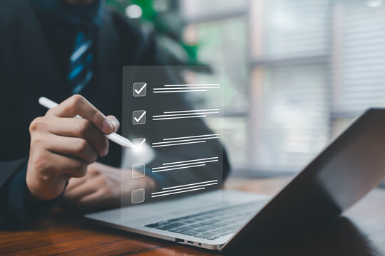 A businessman using a digital pen to check items on a virtual checklist interface displayed above a laptop, representing workflow efficiency, task management, and modern digital productivity. - Powered by Adobe