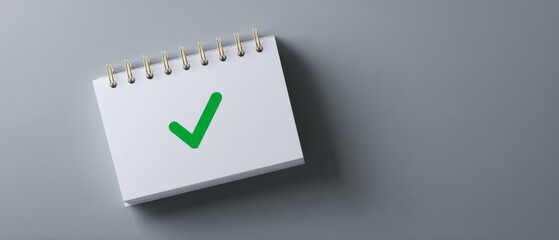 A spiral bound notepad with a green check mark on it is shown against a grey background