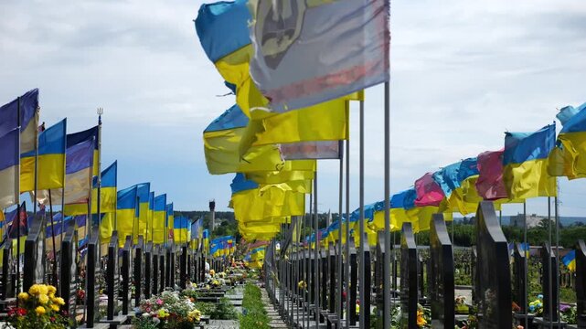 View from window of moving automobile on large military cemetery in Kharkiv with countless graves marked by Ukrainian flags. The site commemorates soldiers who died during russian invasion in Ukraine