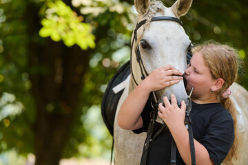 Naklejka premium Girl kissing white horse in nature, showing love and affection, outdoor scene with natural light, friendship and connection, equine therapy concept.