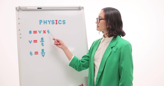 Woman explains distance formula as conducts physics lesson at school. Brunette tutor teaches finding speed and time from problem in classroom