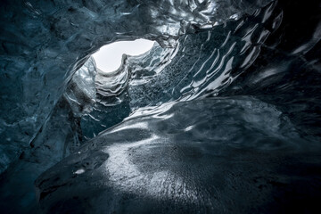 View of ethereal blue ice cave formations sculpted by time and nature, revealing a glimpse of daylight, in Vatnajokull, Iceland.