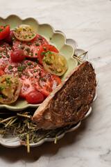 Fresh tomato salad served on a decorative plate. Sliced red and yellow heirloom tomatoes drizzled with olive oil, spices, and herbs, topped with finely chopped chives