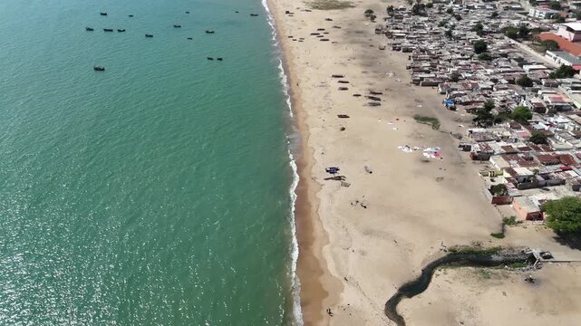 Drone aerial of Benguela, Angola, showing sandy beach, turquoise Atlantic waters, and coastal houses forming a lively urban shoreline under tropical sun