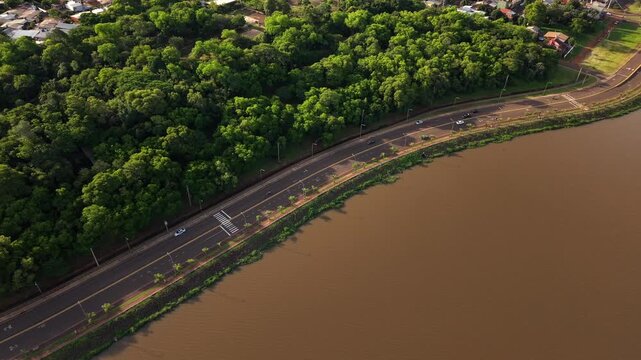 Drone follows light traffic along Avenida Costanera, running between the lush tree canopy of Jard&iacute;n Bot&aacute;nico Alberto Roth and the muddy banks of the Paran&aacute; River, Posadas, Misiones, Argentina.