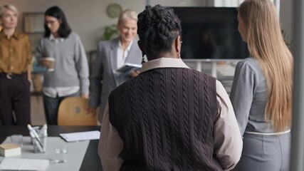 Tracking shot of diverse female team of employees gathering together at conference table with mature Caucasian female CEO greeting everyone and starting business meeting in friendly casual manner - Powered by Adobe