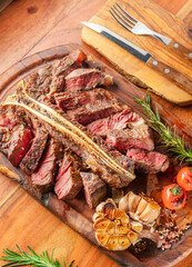 Grilled and sliced T-bone steak with seasonings on slate serving plate. Flat lay.