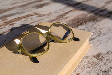 Old-fashioned reading glasses with high optical power lenses for nearsightedness lying on a book in bright sunlight, close-up.