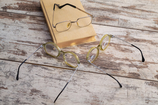 Reading glasses on a book above two pairs of other glasses on a table with light reflections from the lenses, close-up. For illustrating lectures and educational courses, expert opinions