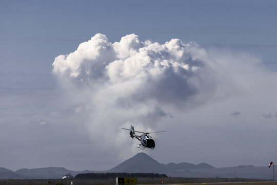 View of a helicopter soaring against the backdrop of towering cumulonimbus clouds and distant mountains, a scene of flight and natural grandeur, Reykjav&iacute;k, Reykjav&iacute;kurborg, Iceland.