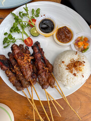 Delicious Grilled Skewers  with Rice, Sambal (Chilli sauce), Pickles and Soy Sauce Plated on Wooden Table Setting