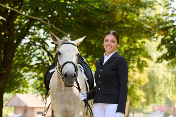 Young woman with her white horse in outdoor setting, equestrian lifestyle, horse riding, horseback riding, animal portrait, nature background, sunny day, happy and smiling.
