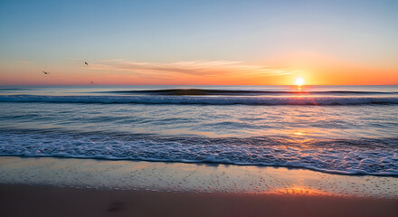 Sunrise on calm ocean with gentle waves, golden sun over horizon, sandy beach