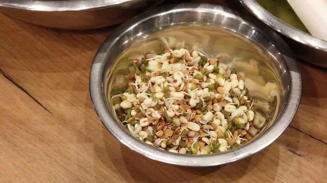 Chopped garlic, shallots, and an assortment of mixed seeds neatly organized from left to right in metal bowls on a kitchen counter, ready for culinary preparation.
