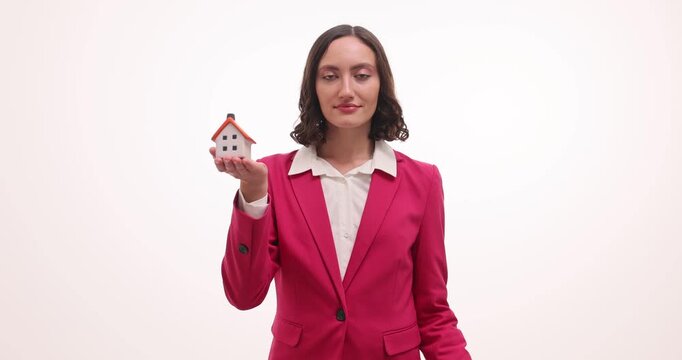 Woman agent in red suit stands in studio holding house model with contract sheet. Lady presents real estate agreement inviting buyer to sign papers