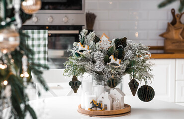Home decoration for the New Year 2026. A bouquet of fir trees with green toys, horses, and white houses on the kitchen table. Christmas decorations in the interior.