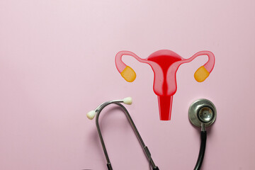 Gynecology and women's health concept. Uterus and ovaries icon with stethoscope on pink background, representing reproductive system care, medical check-up, fertility, and cancer prevention.
