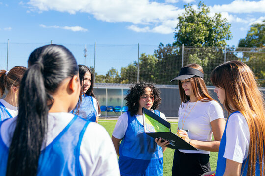 Female coach discussing game plan with soccer players on the field, showing strong teamwork and sport coaching