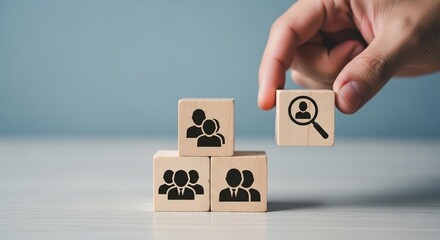Hand placing a wooden block with a magnifying glass icon on top of other blocks with people icons.