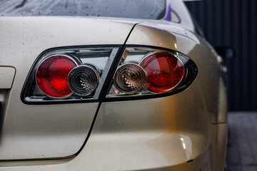 Fototapeta premium Shiny silver car with rain droplets on the headlight, captured in a close-up shot at a brightly lit car wash station