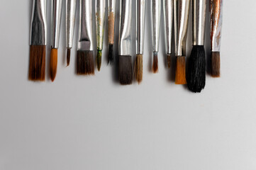 Close up of a group of artist brushes on a white table. The brushes are of different sizes and materials. Art supplies