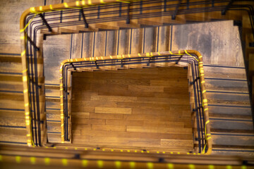 Top-down view of a spiral wooden staircase with warm lighting and black metal railings, forming a geometric composition.