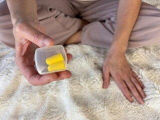 Close-up of a woman&rsquo;s hand holding soft yellow foam earplugs designed for sleep improvement, noise reduction, and hearing protection