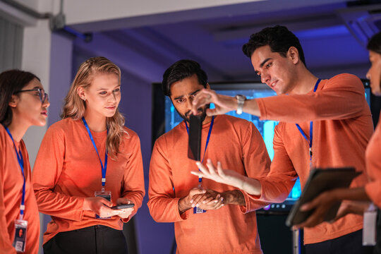 A diverse team of young innovators in a tech lab presents a new smartphone prototype, enthusiastically brainstorming its next-generation design and user interface for a future product launch.