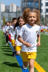 A happy, diverse group of primary school children runs joyfully outdoors in bright sunlight, celebrating friendship, energy, and playful excitement.