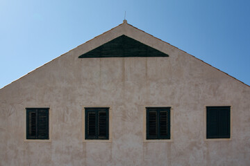 Symmetrical facade of a historic building in Dubrovnik. Four windows with green shutters and a triangular gable against a clear blue sky.