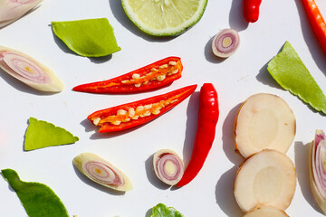 A colorful, close-up pattern of Thai herbs: lime slices, galangal, lemongrass, chilies, and kaffir lime leaves.