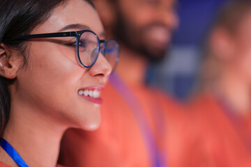 An inspired female tech professional smiles while watching a keynote presentation on innovation at a global technology summit, her eyes reflecting the bright future of the industry.