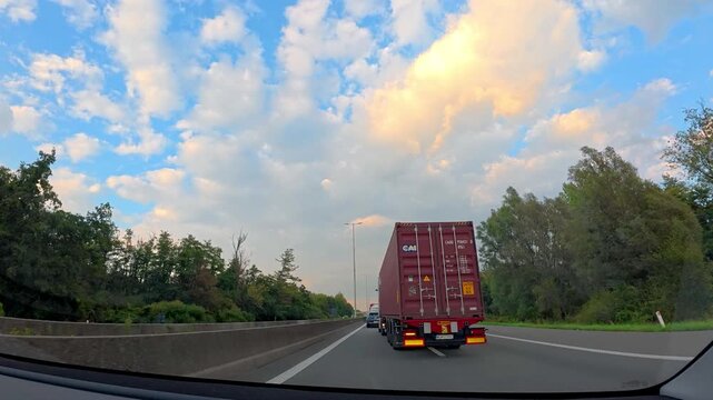 dashcam view highway sunset clouds, golden light bathing passing cars and trucks, smooth asphalt lanes flanked
