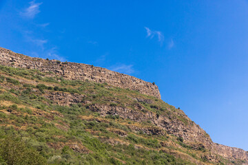 A sunlit mountain landscape featuring a rocky cliff and layered rock. Armenia