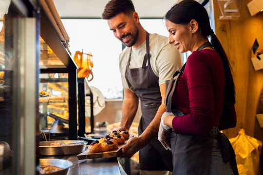 Smiling male and female bakers arranging pastries in a bakery.