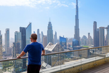 Man enjoying the stunning skyline view of Dubai skyline with Burj Khalifa in the background from high-rise balcony. Modern architecture, skyscrapers, and urban lifestyle