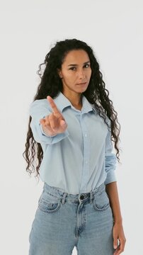 Strict young woman wagging finger to say no. Serious female model showing warning, prohibition or scolding gesture isolated on white background.