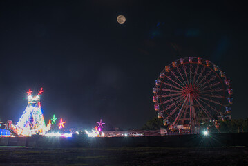 Vibrant rides in the Colorful Giant Ferris wheel with night illumination in the funfair, Maharashtra, India.