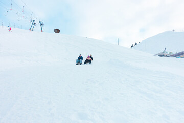 Happy friends having fun with sledding on snow high mountains - Young people enjoy white week vacation - Winter sport and travel concept - Soft focus on guys faces