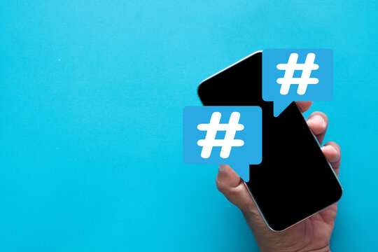Social media trend and viral topic concept. Hand holding smartphone with hashtag icons,symbolizing online marketing,popular discussion, and digital communication on a blue background with copy space.