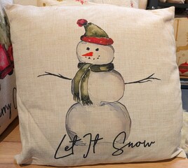 Cojín con dibujo de muñeco de nieve con texto Let it Snow en estante de comercio