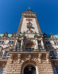 The impressive clock tower and main entrance of Hamburg City Hall in Germany, captured on a clear, sunny day against a bright blue sky