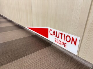 Close up of a "Caution Slope" sign fixed on a wall inside a building